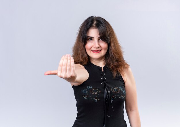 Pretty woman in black blouse smiling on camera calling to her with hand 