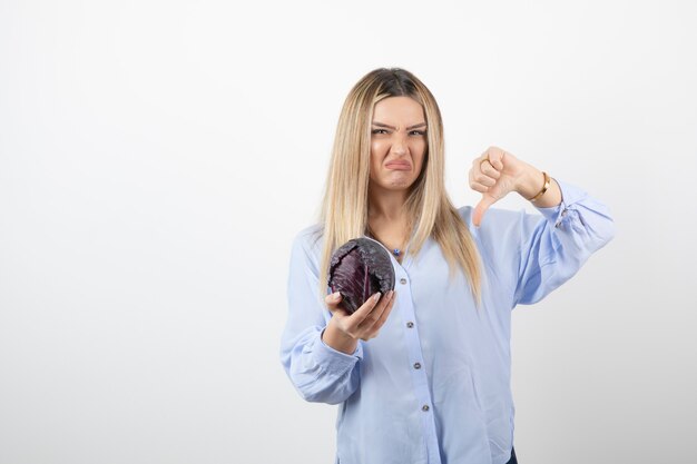 Pretty woman in blue outfit posing with single cabbage on white.