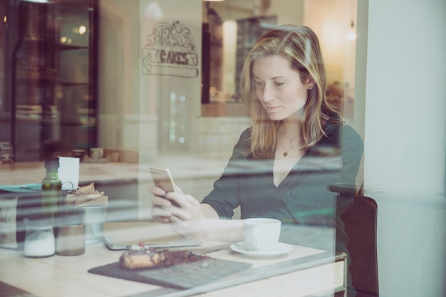 Foto gratuita donna graziosa che passa in rassegna smartphone in caffè piacevole