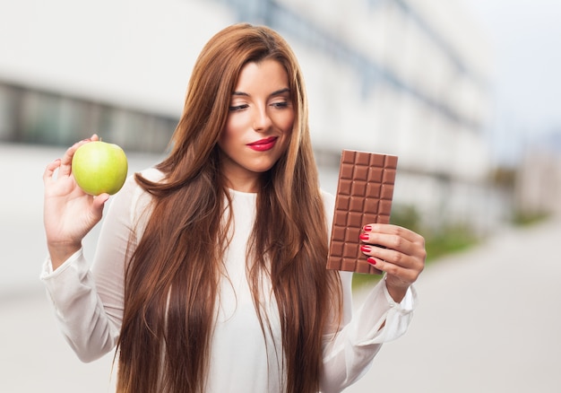 Pretty woman choosing between chocolate and apple