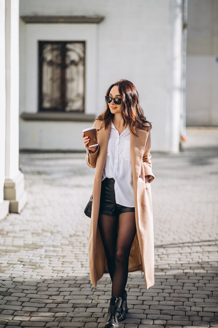 Free Photo pretty woman in coat drinking coffee outside in the street