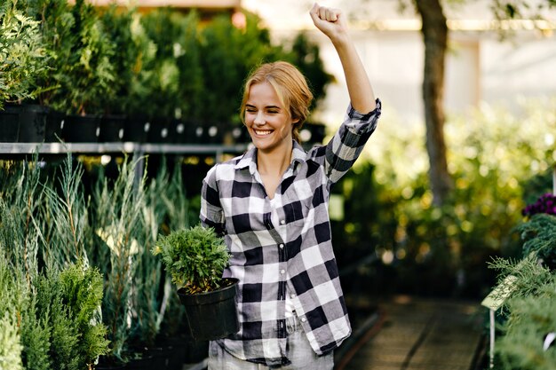 Pretty woman in cute clothes reaching for plants in greenhouse