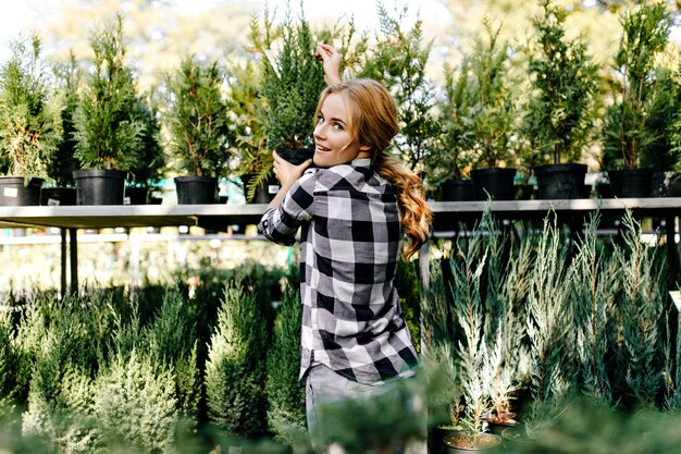 Pretty woman in cute clothes reaching for plants in greenhouse