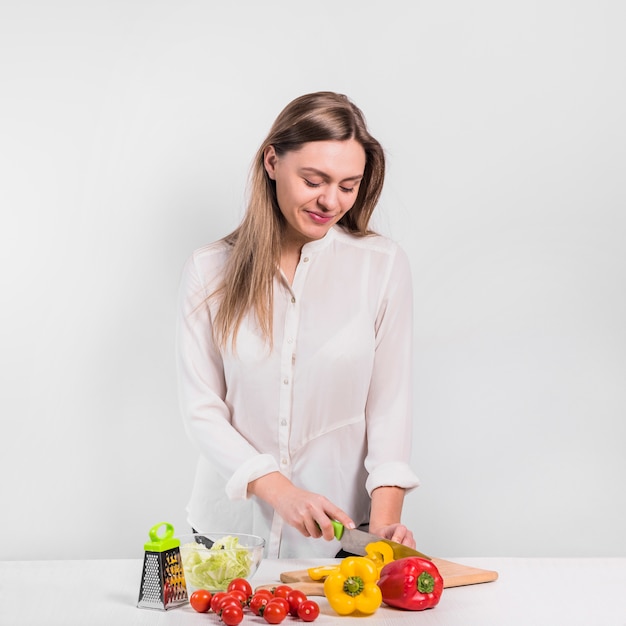 Pretty woman cutting yellow pepper on wooden board