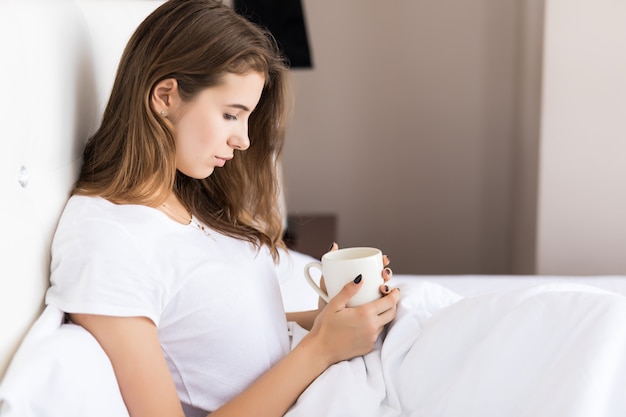 Pretty woman enjoys her morning coffee tea in bed after wake up