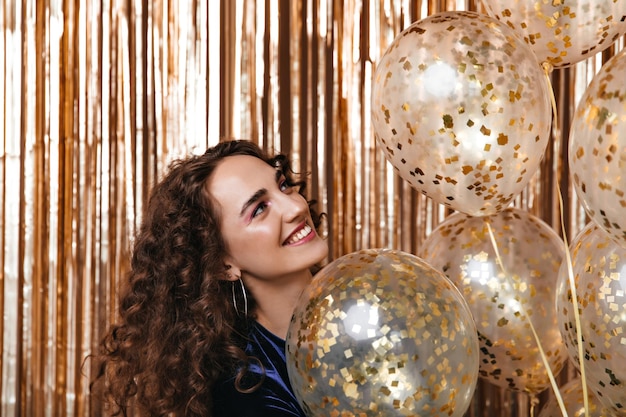 Pretty woman in good mood holding gold balloons