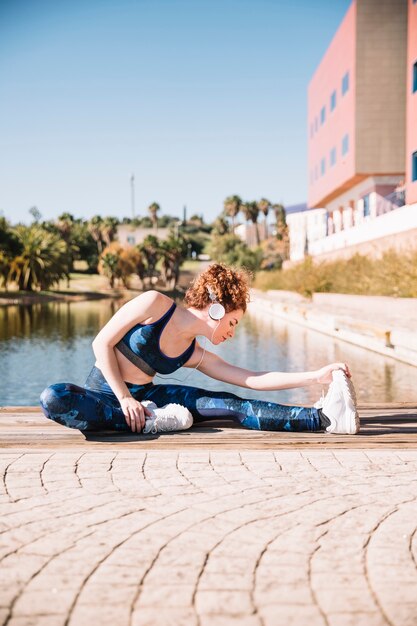 Pretty woman in headphones stretching on pier