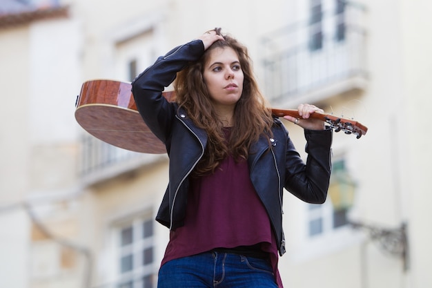 Pretty woman holding guitar sulla spalla sulla strada