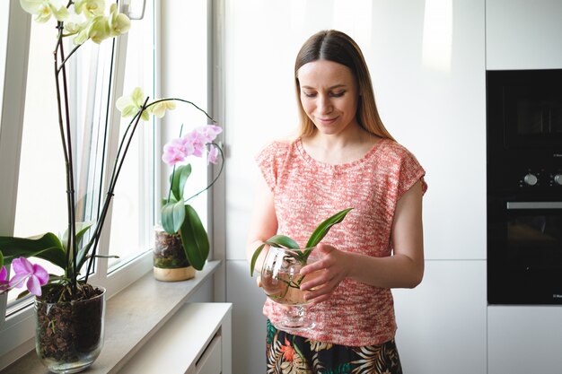 Pretty woman holding in hands a can of water with an orchid plant