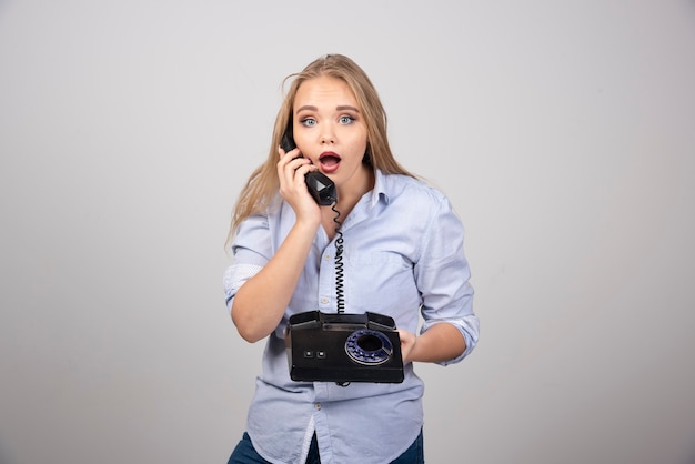 pretty woman holding phone and talking isolated gray wall.