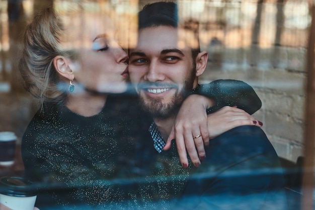 Красотка целует своего улыбающегося мужчину, который смотрит в окно.