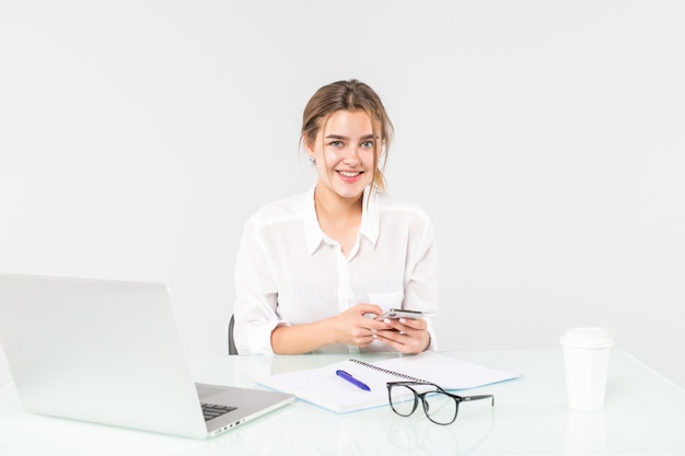 Pretty woman is working at a laptop and reading a message on her phone isolated on white background