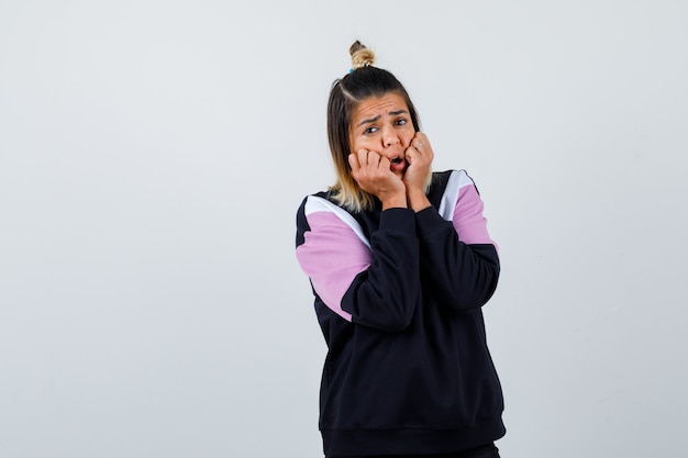 Pretty woman keeping hands near mouth in sweatshirt and looking horrified