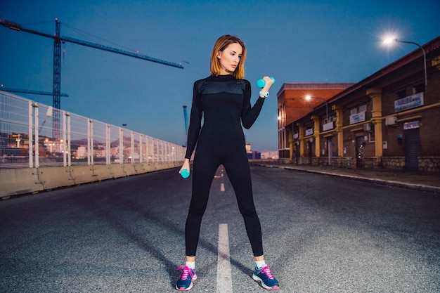 Pretty woman lifting dumbbells on road