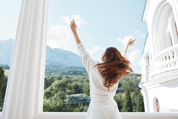 ホテル​の​山​の​景色​の​バルコニー​に​滞在している​白い​バスローブ​で​きれいな​女性​の​長い​髪