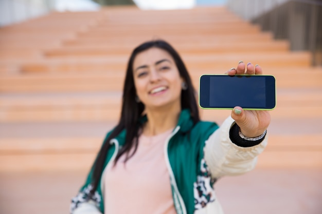 Donna graziosa che fa selfie sul telefono, sorridente. gadget a fuoco