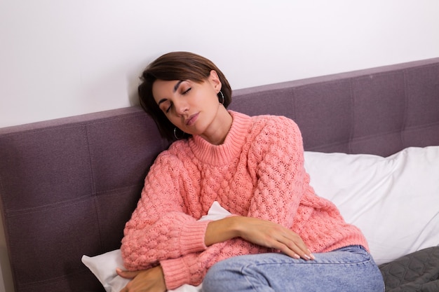 Pretty woman in pink cute knitted pullover resing at home in bed, smiling, enjoying time alone