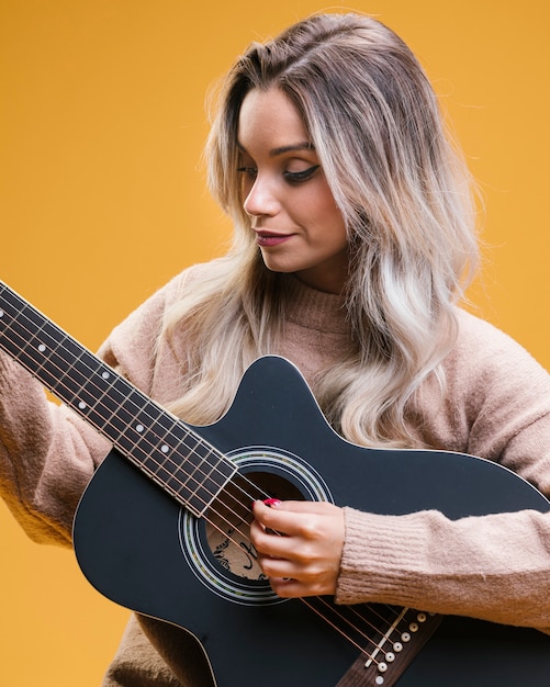 黄色の背景に対してギターを弾くきれいな女性