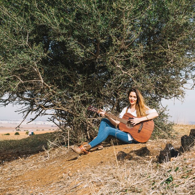 Pretty woman playing guitar near bush