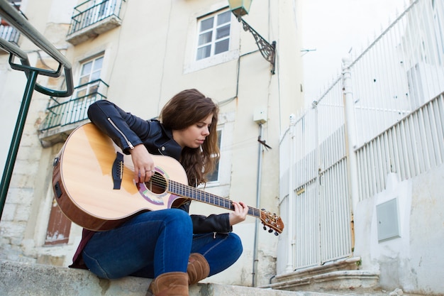 Foto gratuita donna graziosa che gioca chitarra sulle scale della via