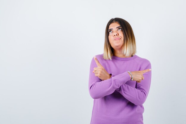 Pretty woman pointing to the both sides, looking up in purple sweater and looking indecisive. front view.