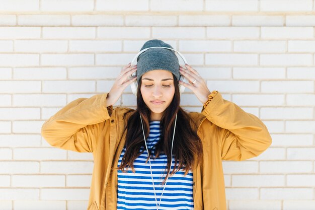 pretty woman standing against white brick wall wearing headphones