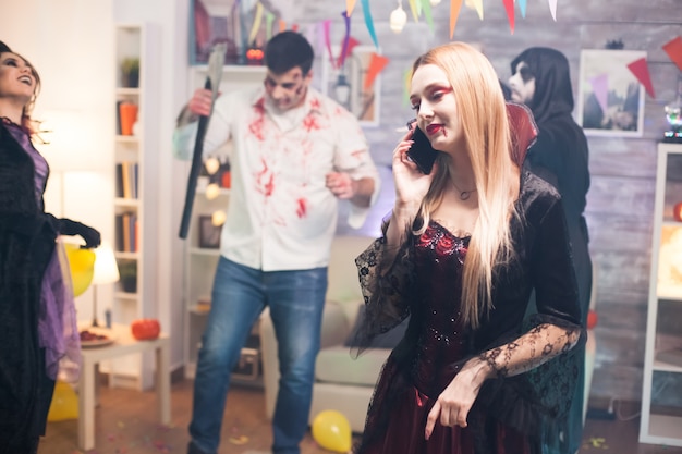 Pretty woman talking on the phone at halloween party dressed up like a vampire.