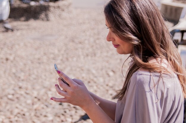 Donna graziosa utilizzando il suo telefono cellulare mentre seduto sulla panca di legno. stile casual - jeans e camicia. felice giovane donna utilizzando smartphone in una giornata di sole