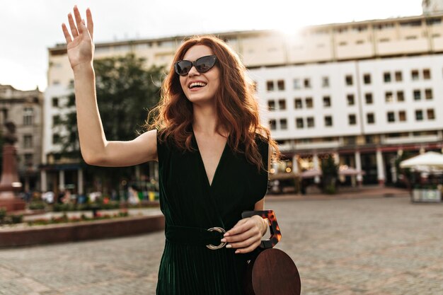 Pretty woman in velvet dress holds handbag and waving hand