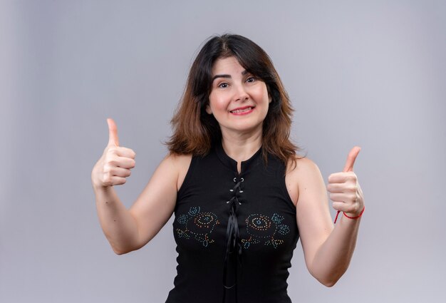 Pretty woman wearing black blouse doing happy thumbs up over gray background
