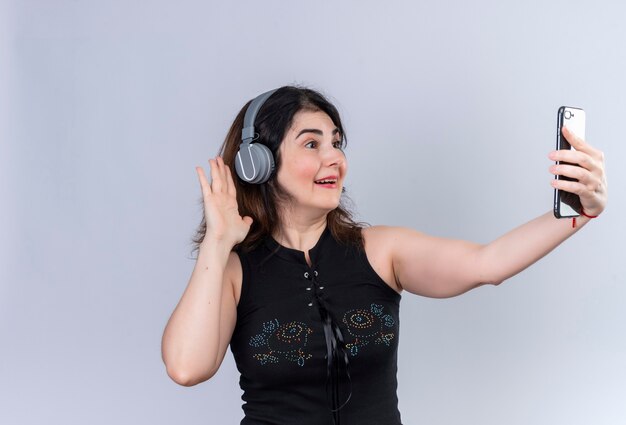 Pretty woman wearing black blouse greeting someone in phone wearing headphones 