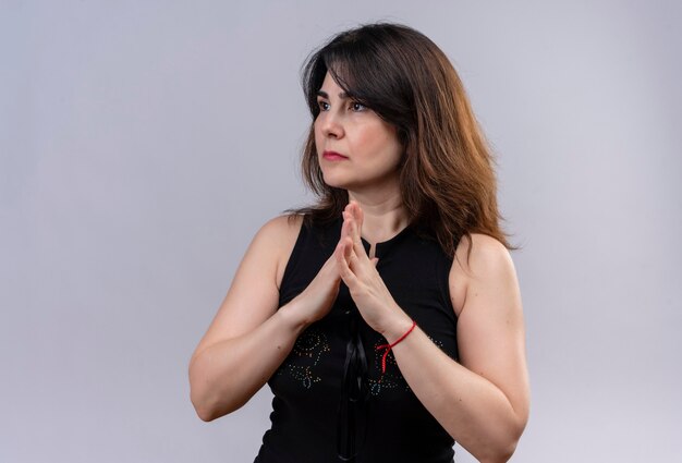 Pretty woman wearing black blouse looking besides awaiting joined her hands