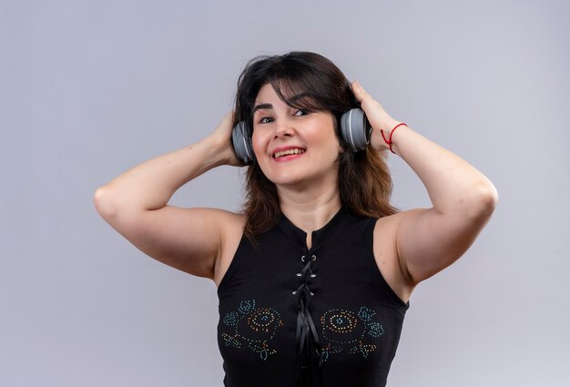 Pretty woman wearing black blouse looking energetic listening to music with headphones