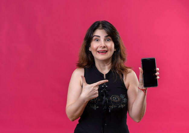 Pretty woman wearing black blouse looking  happily pointing at the phone