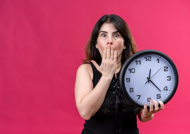 Pretty woman wearing black blouse looking  scared holding clock