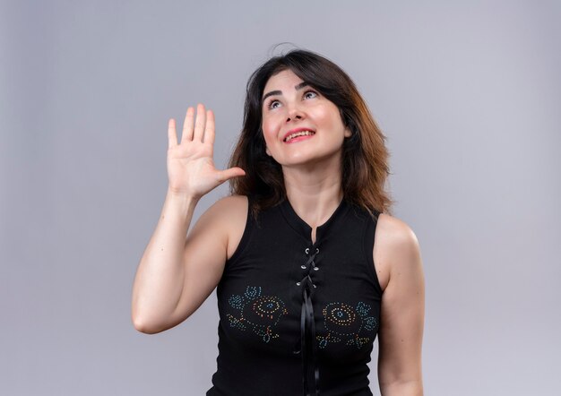 Pretty woman wearing black blouse looking up calling someone with hand