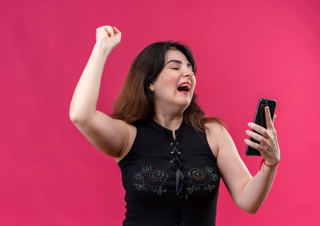 Pretty woman wearing black blouse looks rejoicing on phone