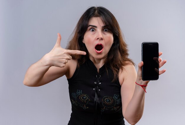 Pretty woman wearing black blouse shocked pointing at phone