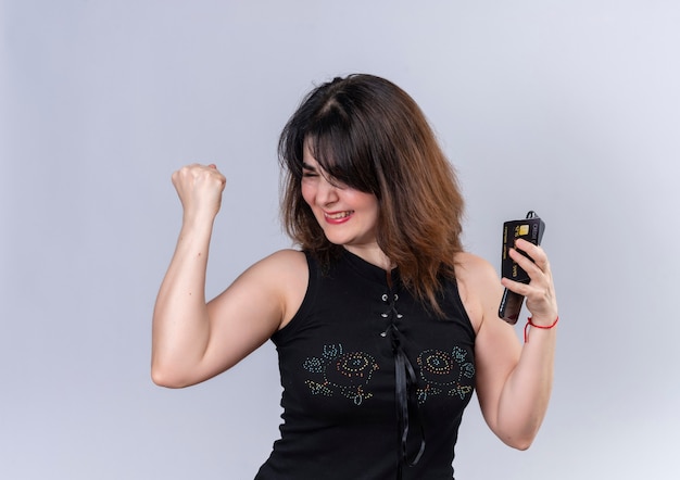 Pretty woman wearing black blouse showing happiness with did it sign holding phone and card