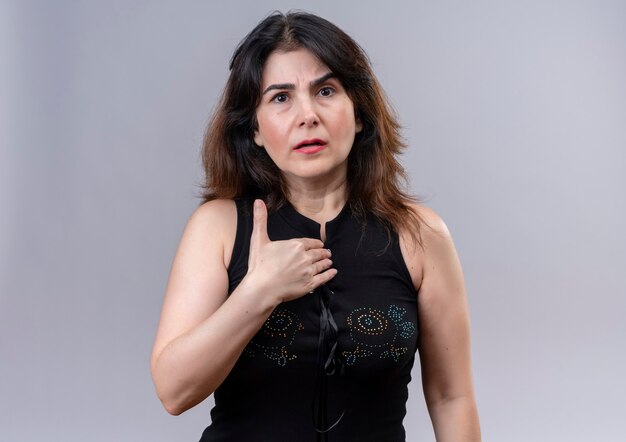 Pretty woman wearing black blouse  with reproachful face points at herself standing over pogray background