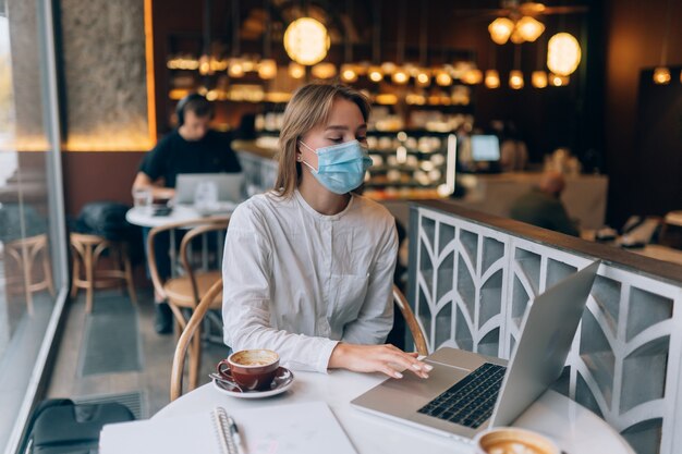 仕事にラップトップを使用して医療用フェイスマスクを身に着けているきれいな女性