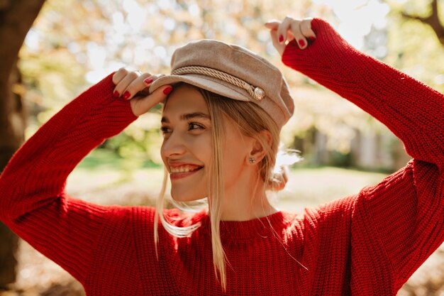 Pretty woman wearing trendy accessories in the autumn. Closeup photo of a smiling blonde in the park.