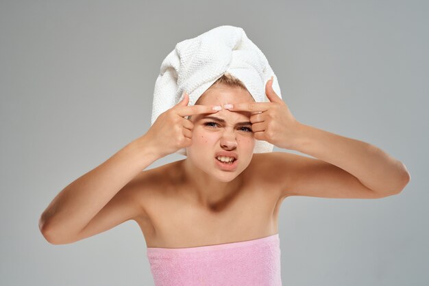 裸​の​肩​を​持つ​きれいな​女性​は​彼女​の​顔​の​皮膚​の​問題​に​にきび​を​絞る