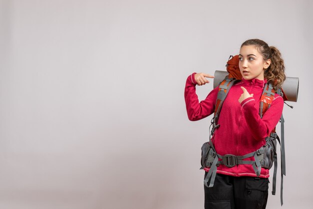 pretty woman with big backpack pointing at herself standing on grey