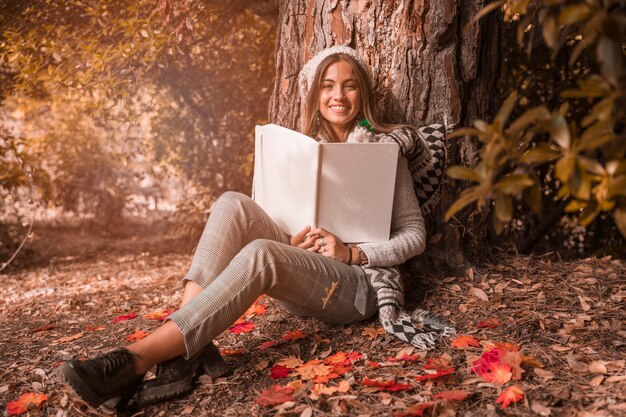 木の近くに座って本を持つかわいい女性