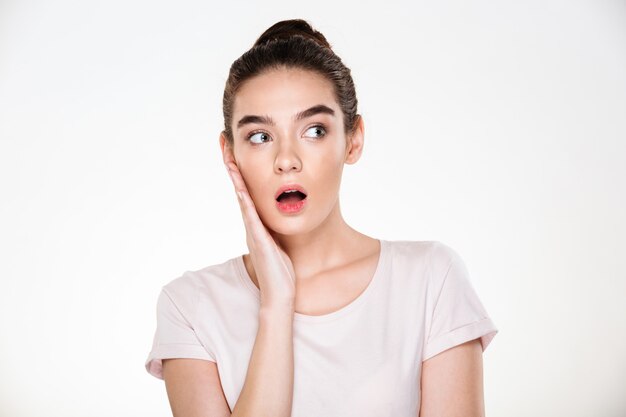 Pretty woman with brown hair in bun touching her face expressing surprise or shock posing