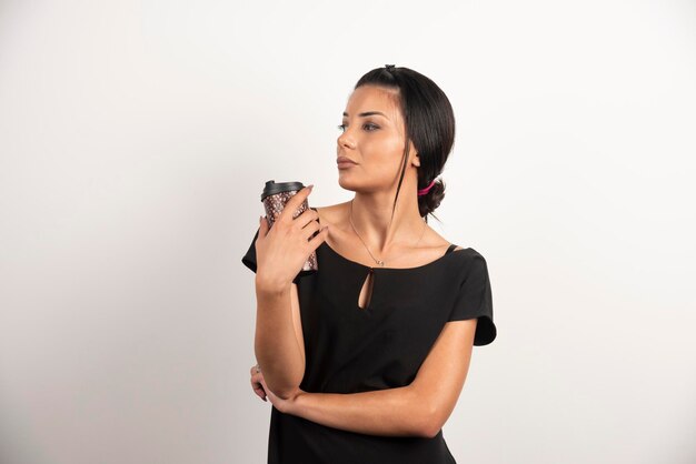 Pretty woman with cup of coffee standing on white wall.