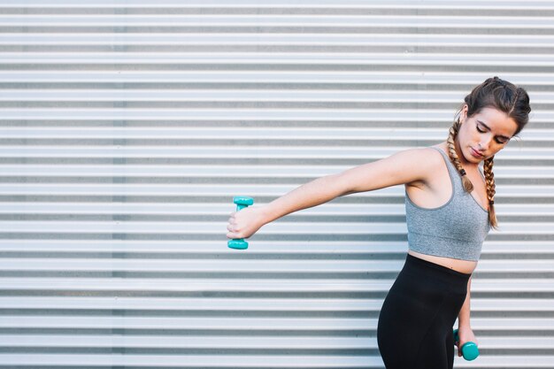 Pretty woman with dumbbells at fence