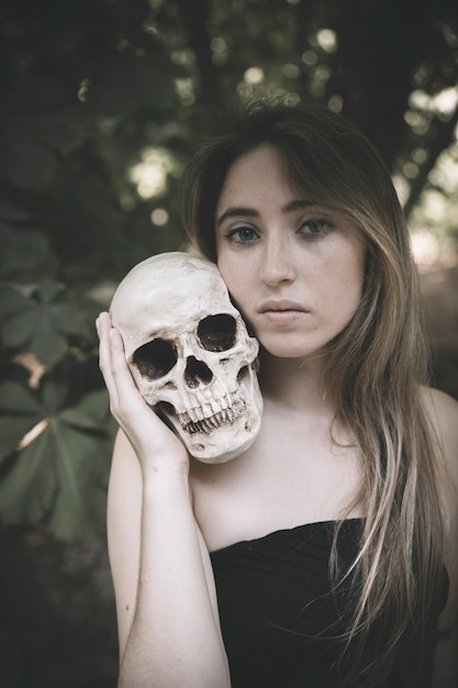 Pretty woman with human skull in forest