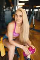 Free photo pretty woman with long blond hair relaxing in the gym with a pink bottle of water